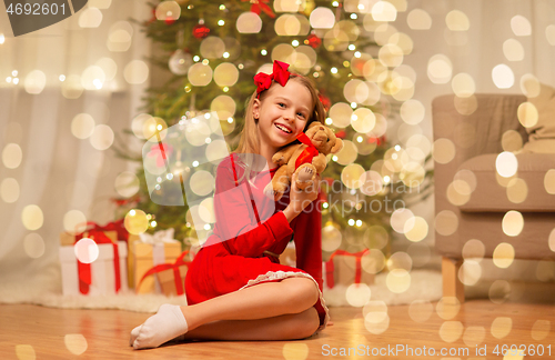 Image of girl in red dress hugging teddy bear at home