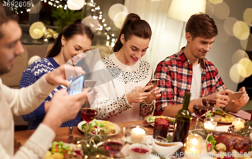 Image of friends with smartphones having christmas dinner