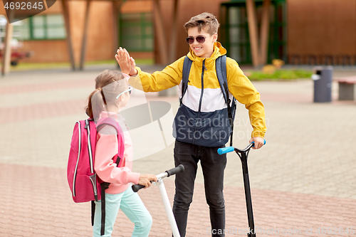 Image of happy school children with backpacks and scooters