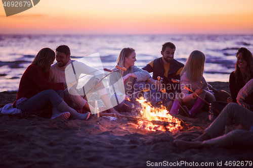 Image of Group Of Young Friends Sitting By The Fire at beach