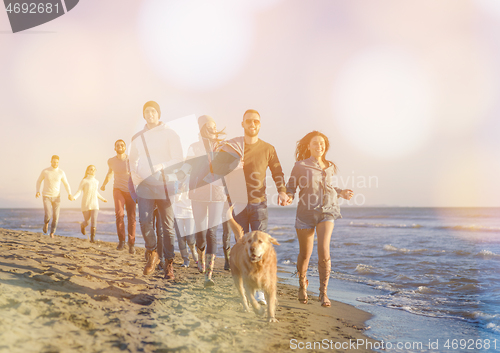 Image of Group of friends running on beach during autumn day