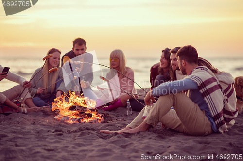 Image of Group Of Young Friends Sitting By The Fire at beach