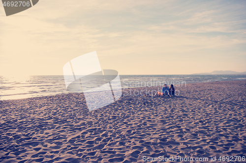 Image of Young Couple Sitting On The Beach beside Campfire drinking beer