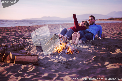 Image of Young Couple Sitting On The Beach beside Campfire drinking beer