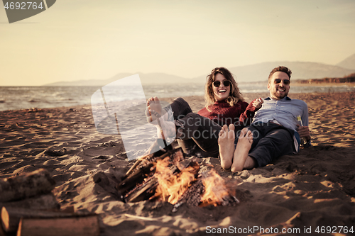 Image of Young Couple Sitting On The Beach beside Campfire drinking beer