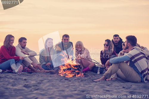 Image of Group Of Young Friends Sitting By The Fire at beach