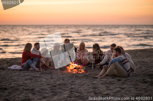 Image of Group Of Young Friends Sitting By The Fire at beach