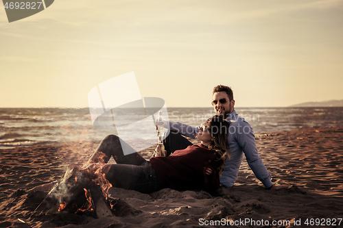 Image of Young Couple Sitting On The Beach beside Campfire drinking beer