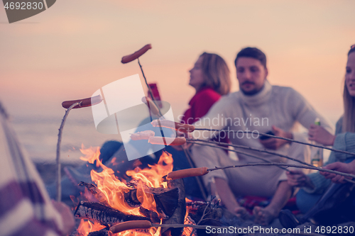 Image of Group Of Young Friends Sitting By The Fire at beach