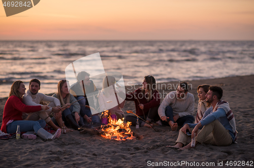 Image of Group Of Young Friends Sitting By The Fire at beach