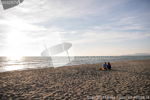 Image of Young Couple Sitting On The Beach beside Campfire drinking beer