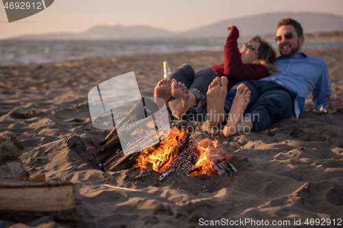 Image of Young Couple Sitting On The Beach beside Campfire drinking beer