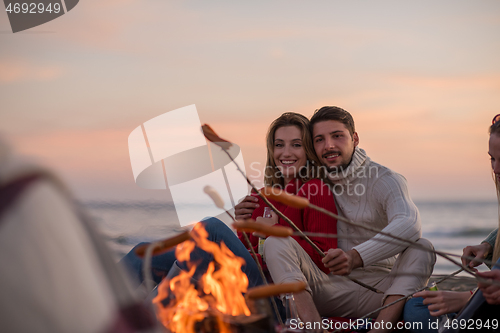 Image of Group Of Young Friends Sitting By The Fire at beach