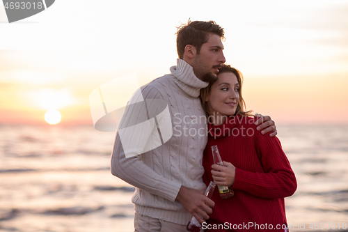 Image of Couple hugging and drinking beer together at the beach