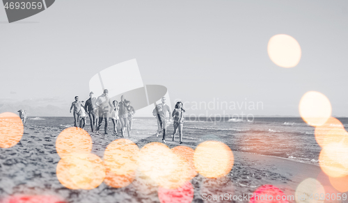 Image of Group of friends running on beach during autumn day