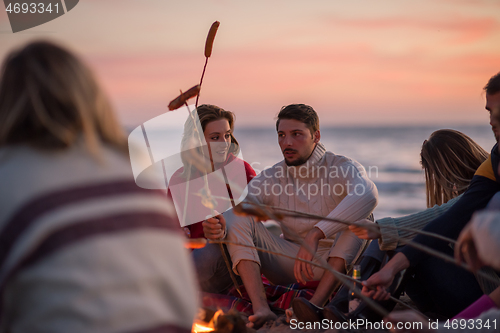 Image of Group Of Young Friends Sitting By The Fire at beach