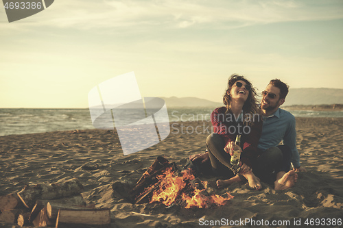 Image of Young Couple Sitting On The Beach beside Campfire drinking beer