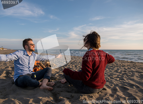 Image of Young Couple Sitting On The Beach beside Campfire drinking beer