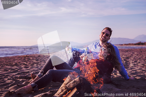 Image of Young Couple Sitting On The Beach beside Campfire drinking beer