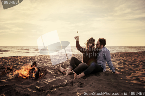 Image of Young Couple Sitting On The Beach beside Campfire drinking beer