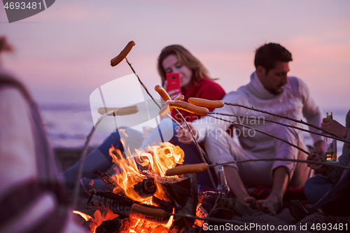 Image of Group Of Young Friends Sitting By The Fire at beach