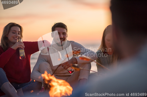 Image of Group Of Young Friends Sitting By The Fire at beach