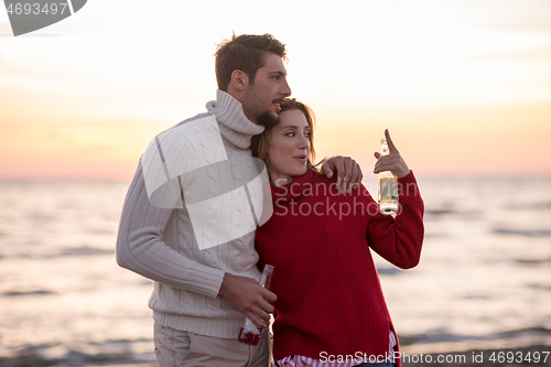 Image of Couple hugging and drinking beer together at the beach