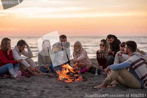 Image of Group Of Young Friends Sitting By The Fire at beach