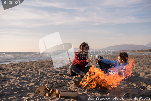 Image of Young Couple Sitting On The Beach beside Campfire drinking beer