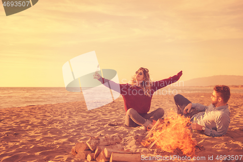 Image of Young Couple Sitting On The Beach beside Campfire drinking beer