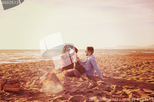 Image of Young Couple Sitting On The Beach beside Campfire drinking beer