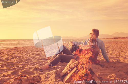 Image of Young Couple Sitting On The Beach beside Campfire drinking beer