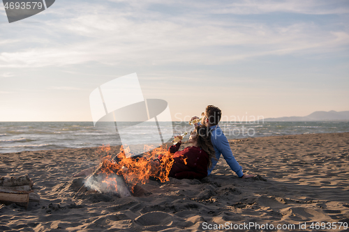 Image of Young Couple Sitting On The Beach beside Campfire drinking beer