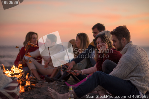 Image of Group Of Young Friends Sitting By The Fire at beach