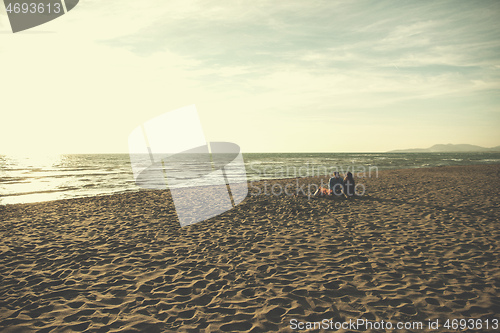 Image of Young Couple Sitting On The Beach beside Campfire drinking beer