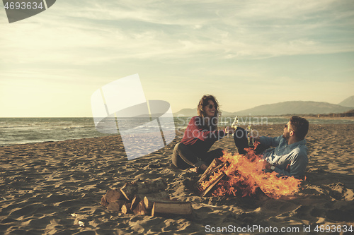 Image of Young Couple Sitting On The Beach beside Campfire drinking beer