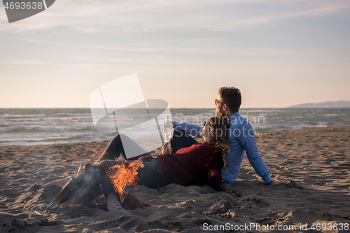 Image of Young Couple Sitting On The Beach beside Campfire drinking beer