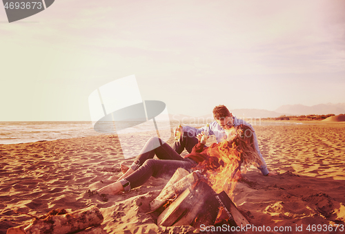 Image of Young Couple Sitting On The Beach beside Campfire drinking beer