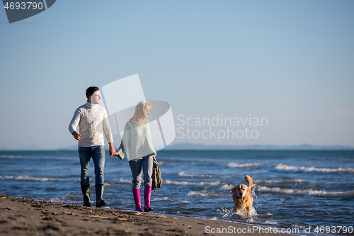 Image of couple with dog having fun on beach on autmun day