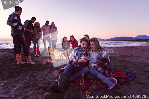 Image of Couple enjoying bonfire with friends on beach