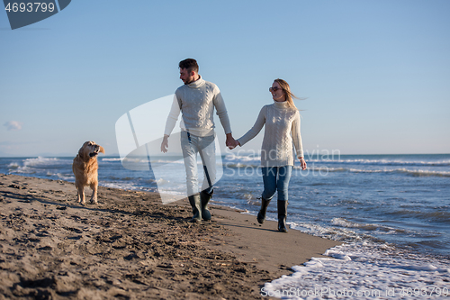 Image of couple with dog having fun on beach on autmun day