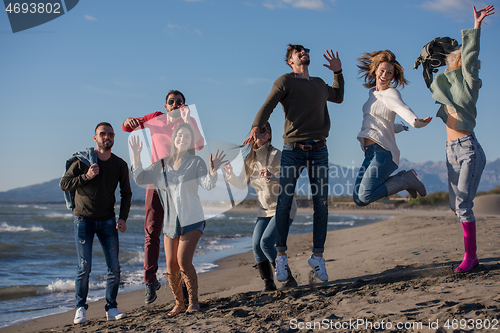 Image of young friends jumping together at autumn beach