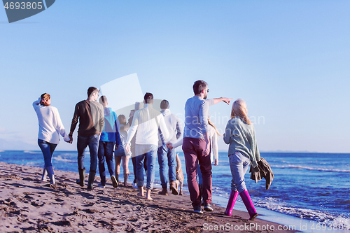 Image of Group of friends running on beach during autumn day