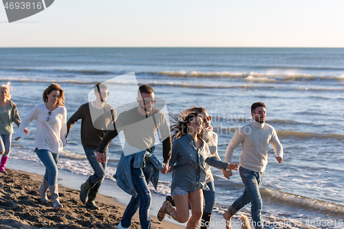 Image of Group of friends running on beach during autumn day