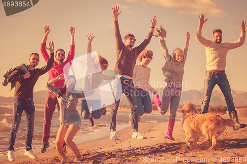 Image of young friends jumping together at autumn beach