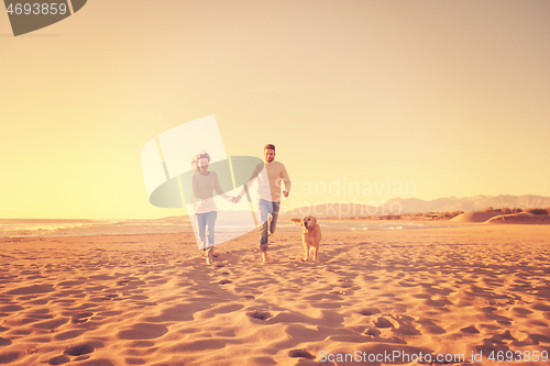 Image of couple with dog having fun on beach on autmun day