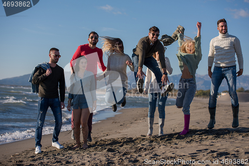 Image of young friends jumping together at autumn beach