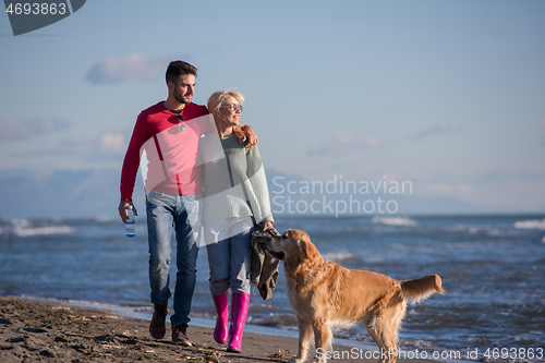 Image of couple with dog having fun on beach on autmun day