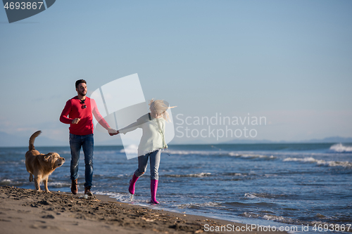 Image of couple with dog having fun on beach on autmun day