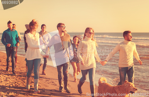 Image of Group of friends running on beach during autumn day